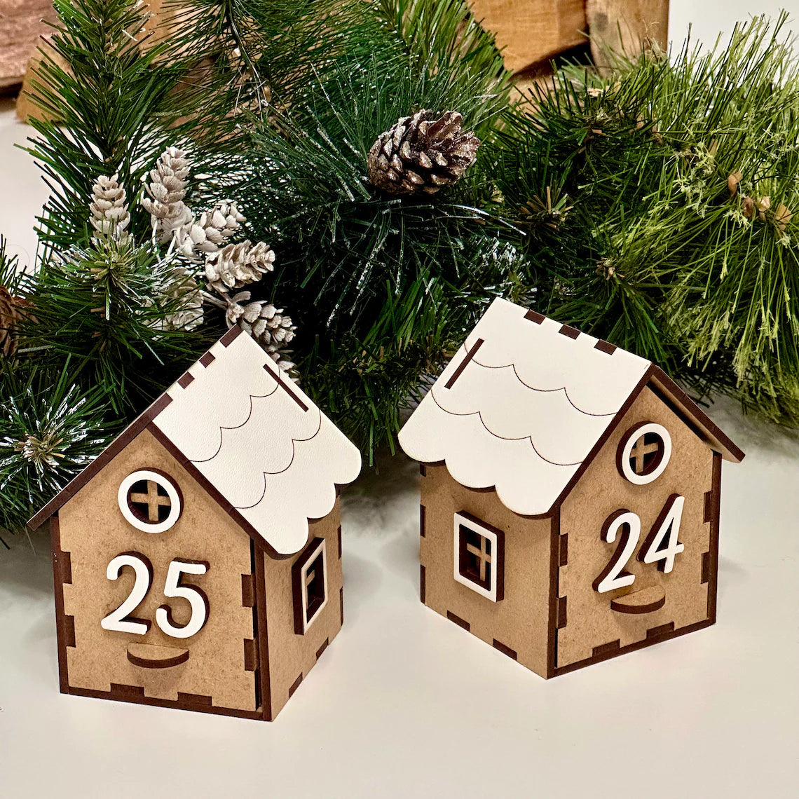 Two wooden house-shaped ornaments with numbers 25 and 24 on a Christmas tree background.