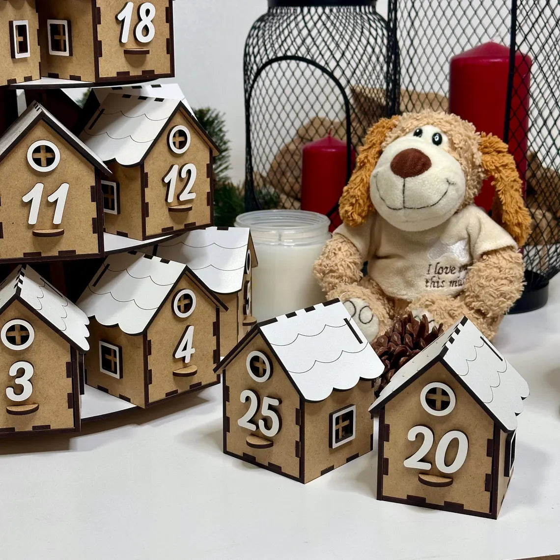Wooden advent calendar houses with numbers, teddy bear, and candles on a white surface.