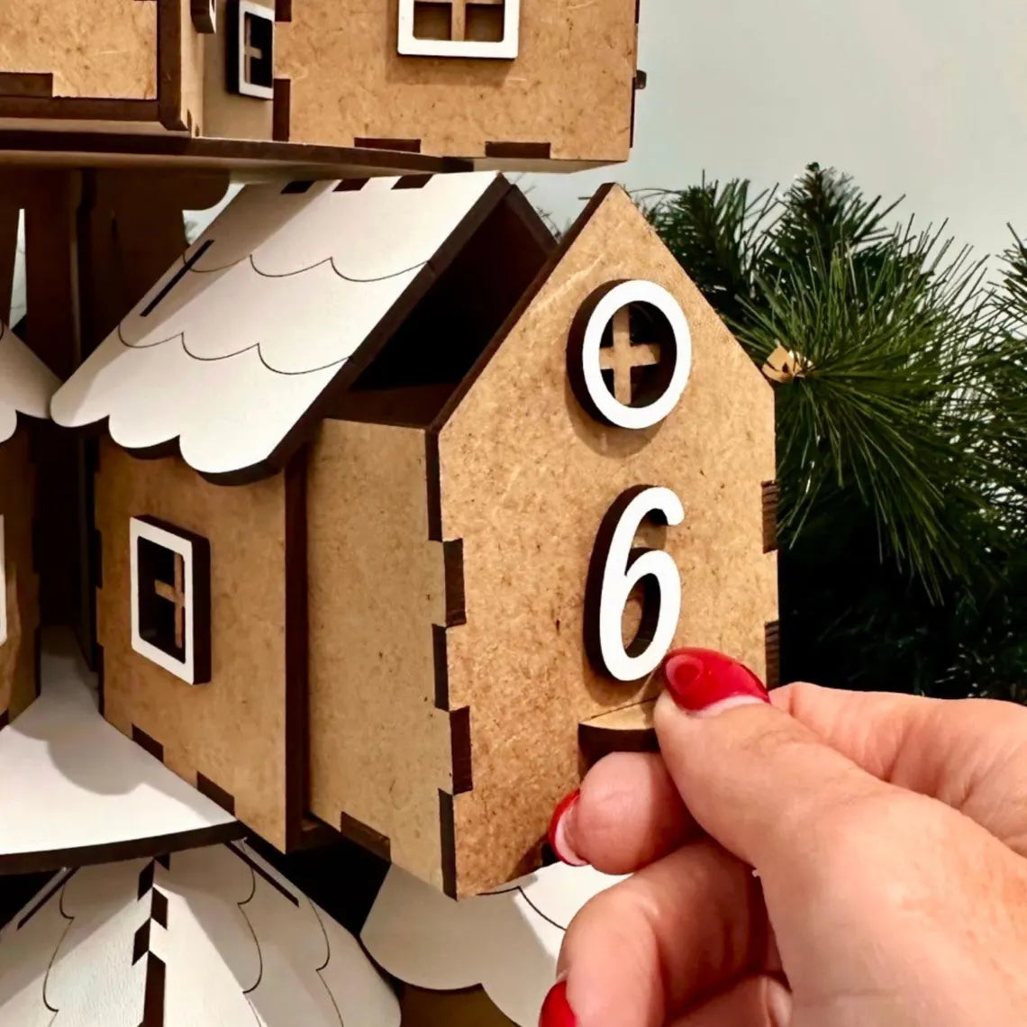 Wooden house model with a hand adjusting a number '6' on it, against a blurred natural background.