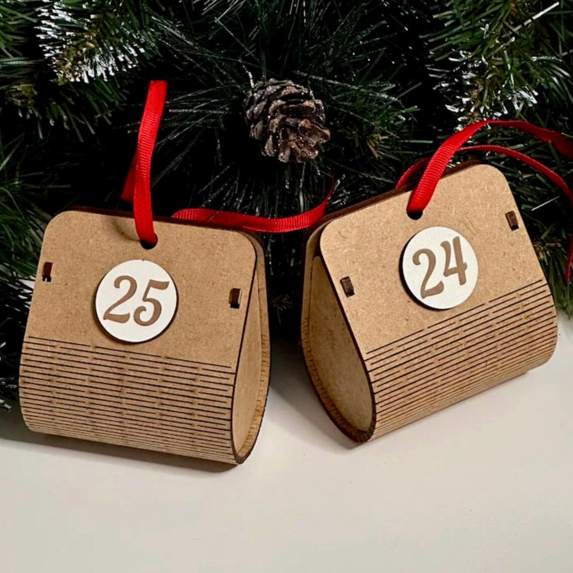 Two cardboard advent calendar pieces with numbers 24 and 25 hanging on a Christmas tree.