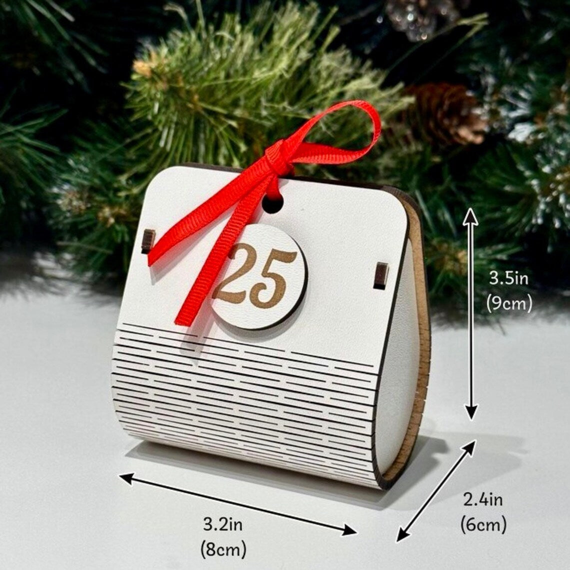 White wooden advent calendar with red ribbon and number 25 tag, Christmas tree in background
