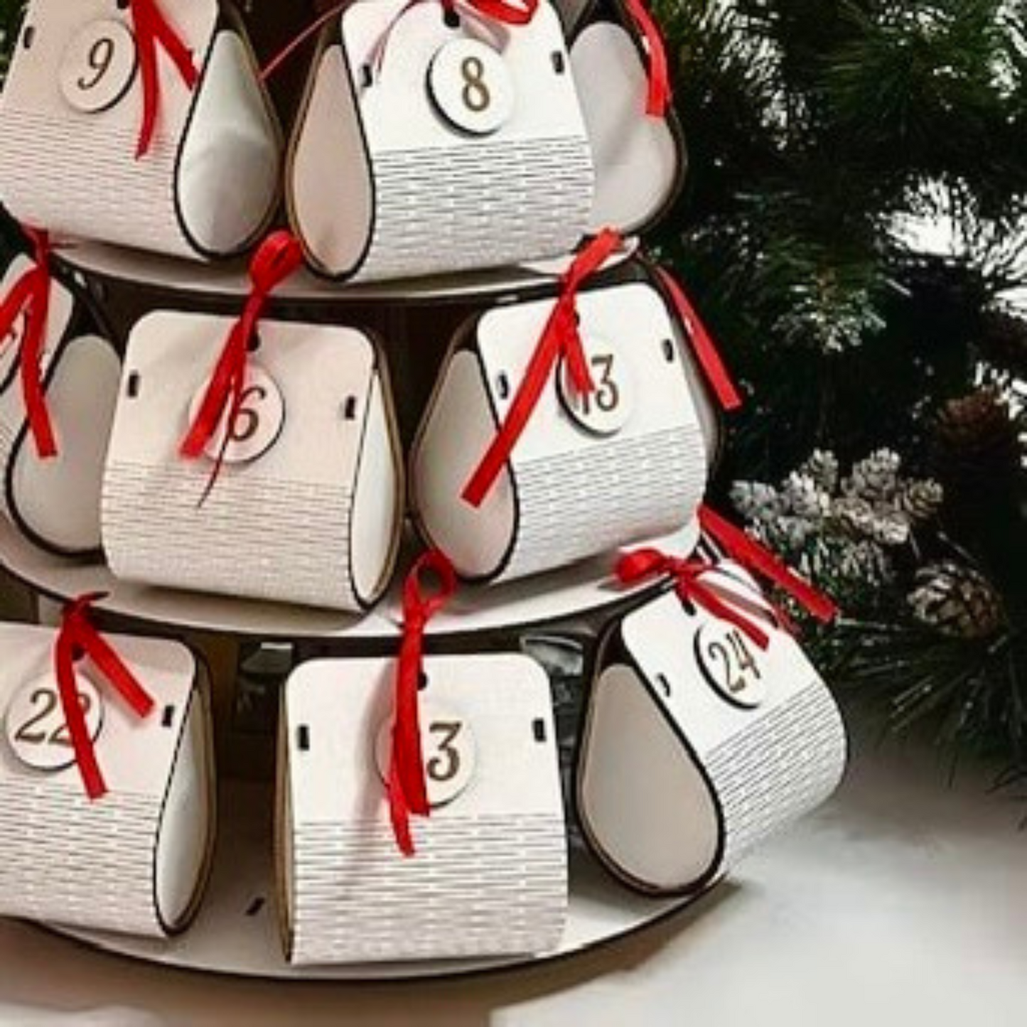 Stack of white cylindrical advent calendar boxes with red ribbons and numbers, against a Christmas tree background.