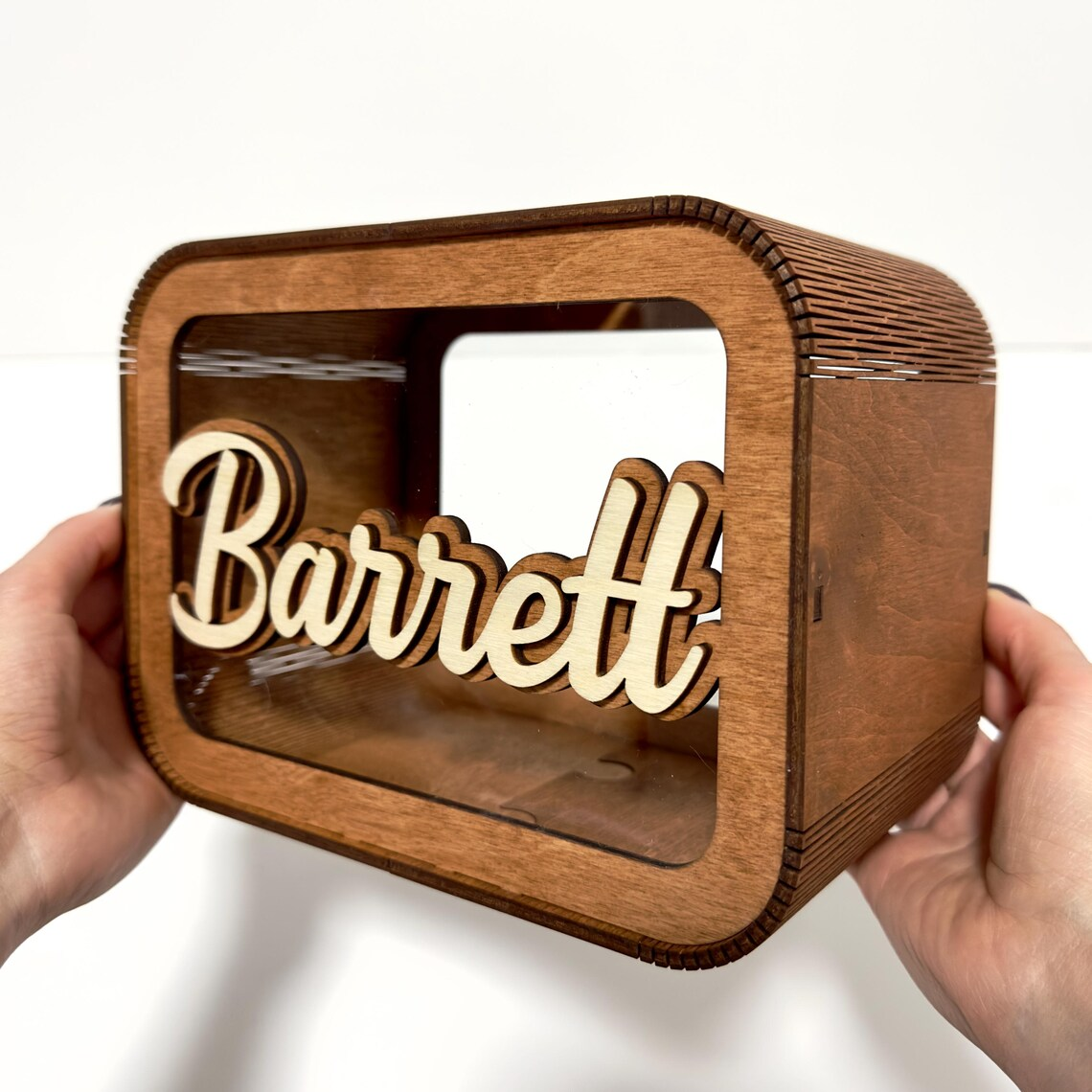 Wooden box with 'Barrett' engraved on it, held by two hands against a white background