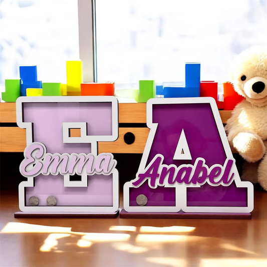 Colorful letter blocks with names 'Emma' and 'Anabel' on a wooden surface with a teddy bear in the background.