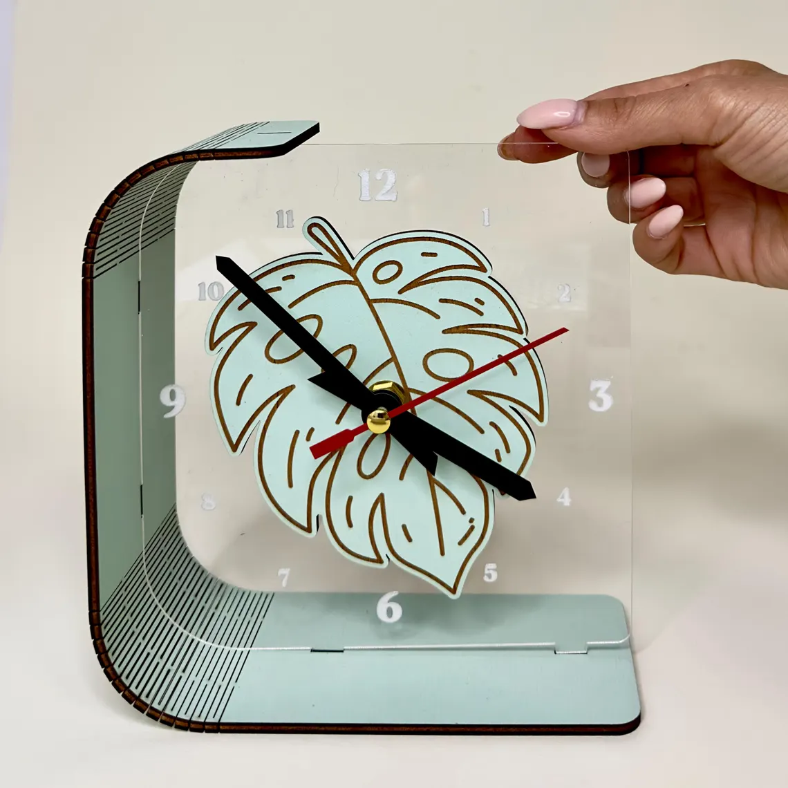 Desk clock with leaf design held by a hand on a light background