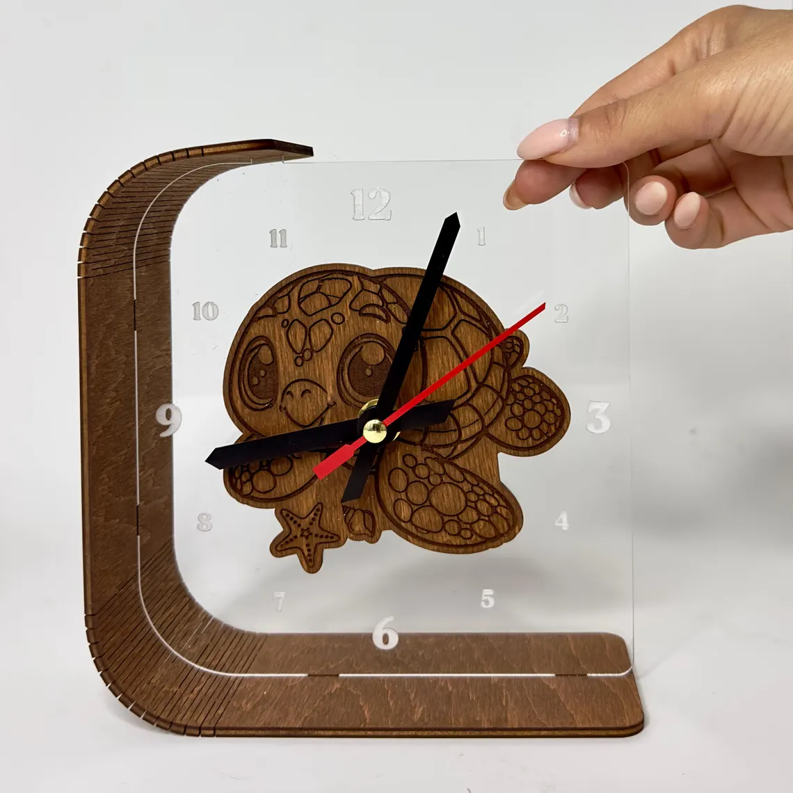Wooden clock with turtle design held by a hand on a white background