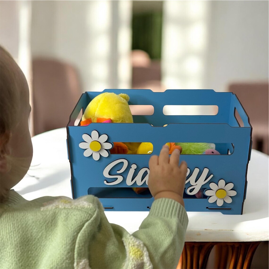 Child playing with a blue toy box labeled 'Sia' on a table.