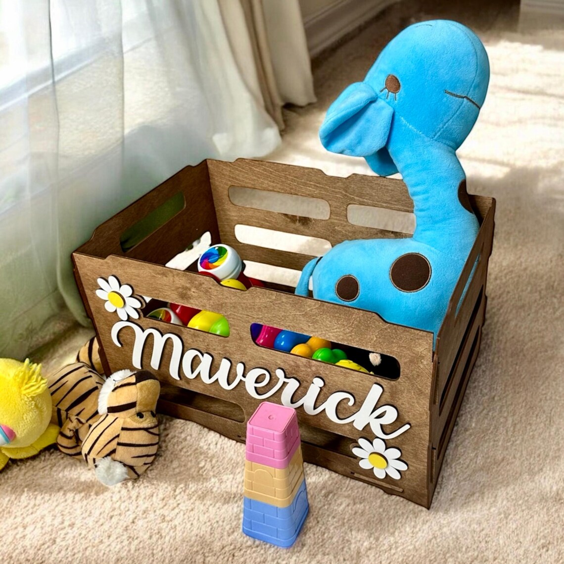 Wooden toy box with personalized name 'Maverick' containing toys on a carpeted floor.