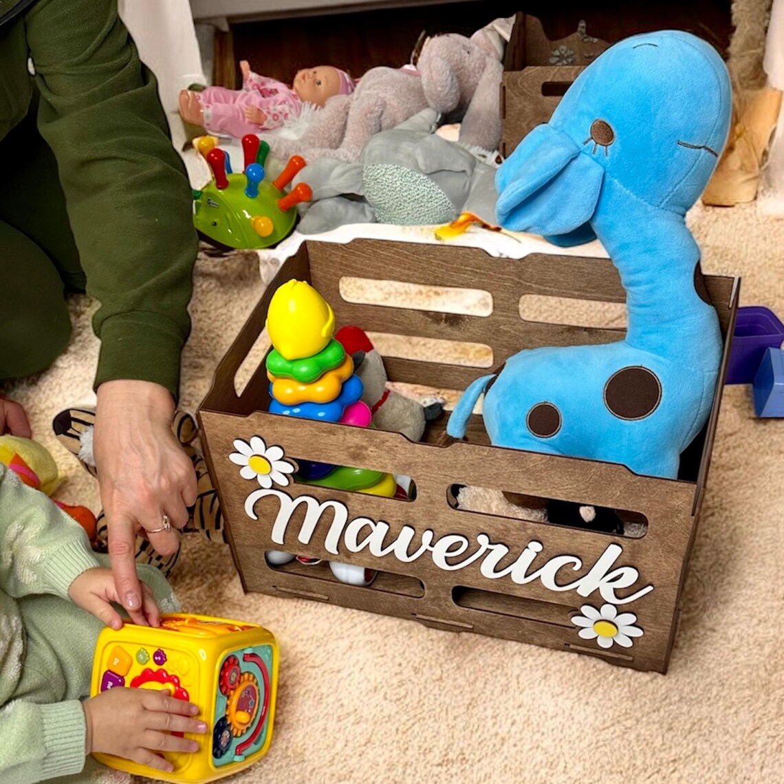 Wooden toy crate with personalized name 'Maverick' filled with toys on a carpeted floor.