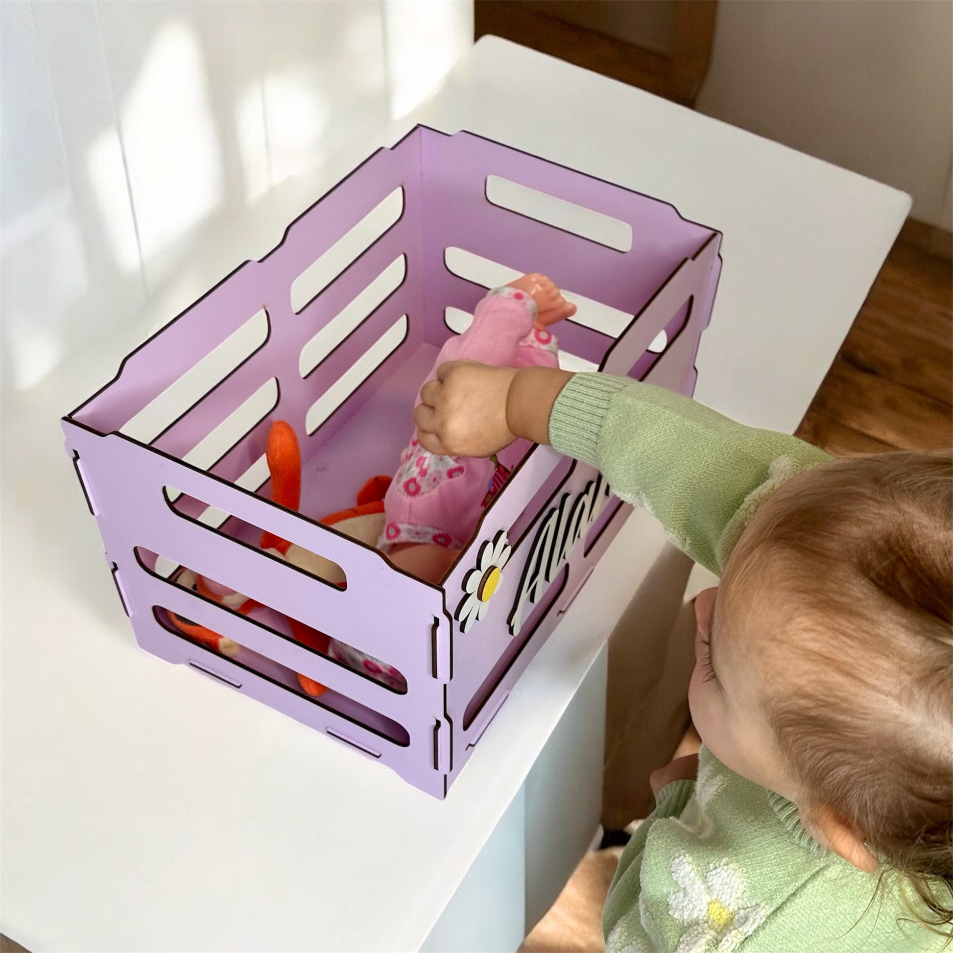 Child playing with toys in a purple crate on a white table.