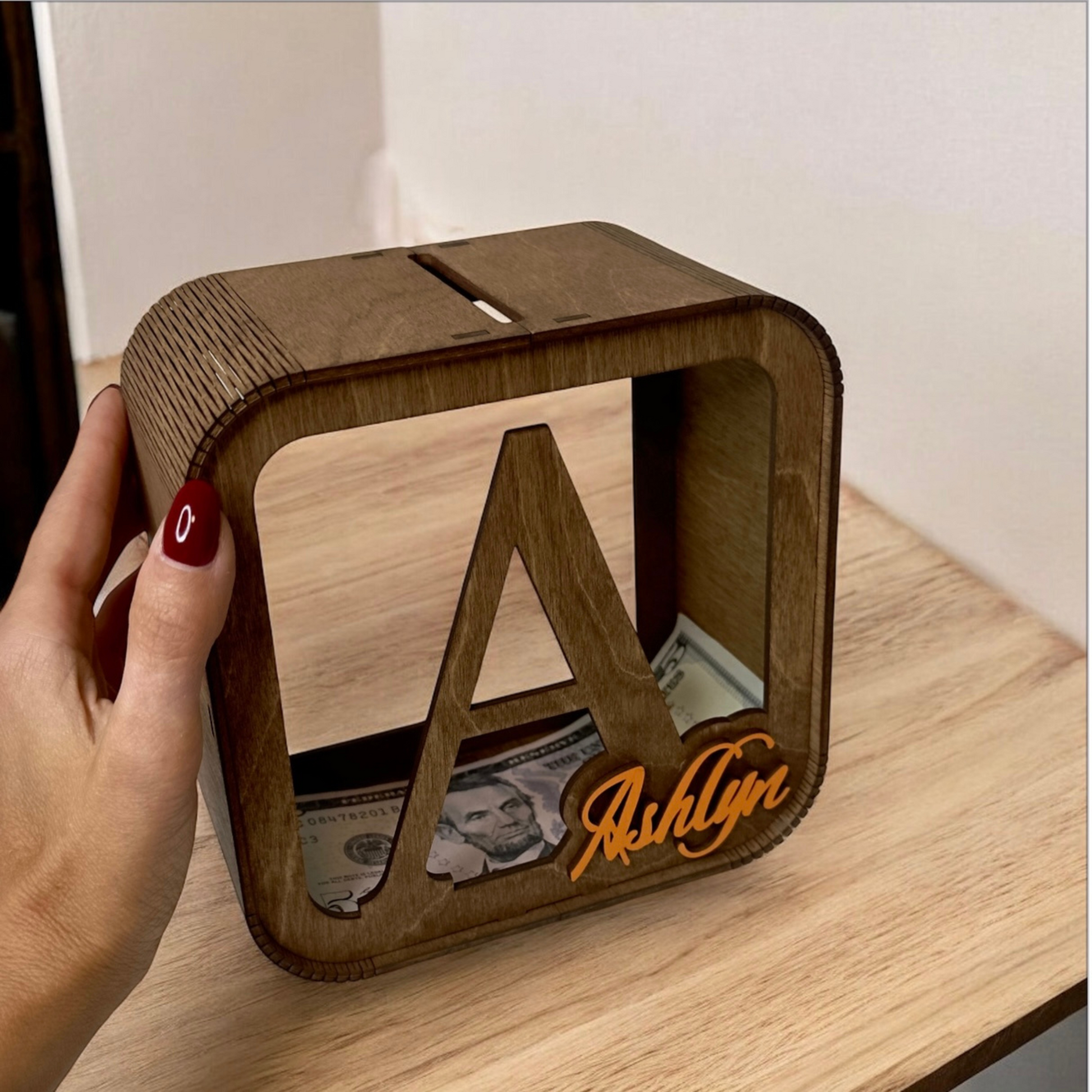 Wooden money box with 'Ashlyn' engraving on a wooden surface
