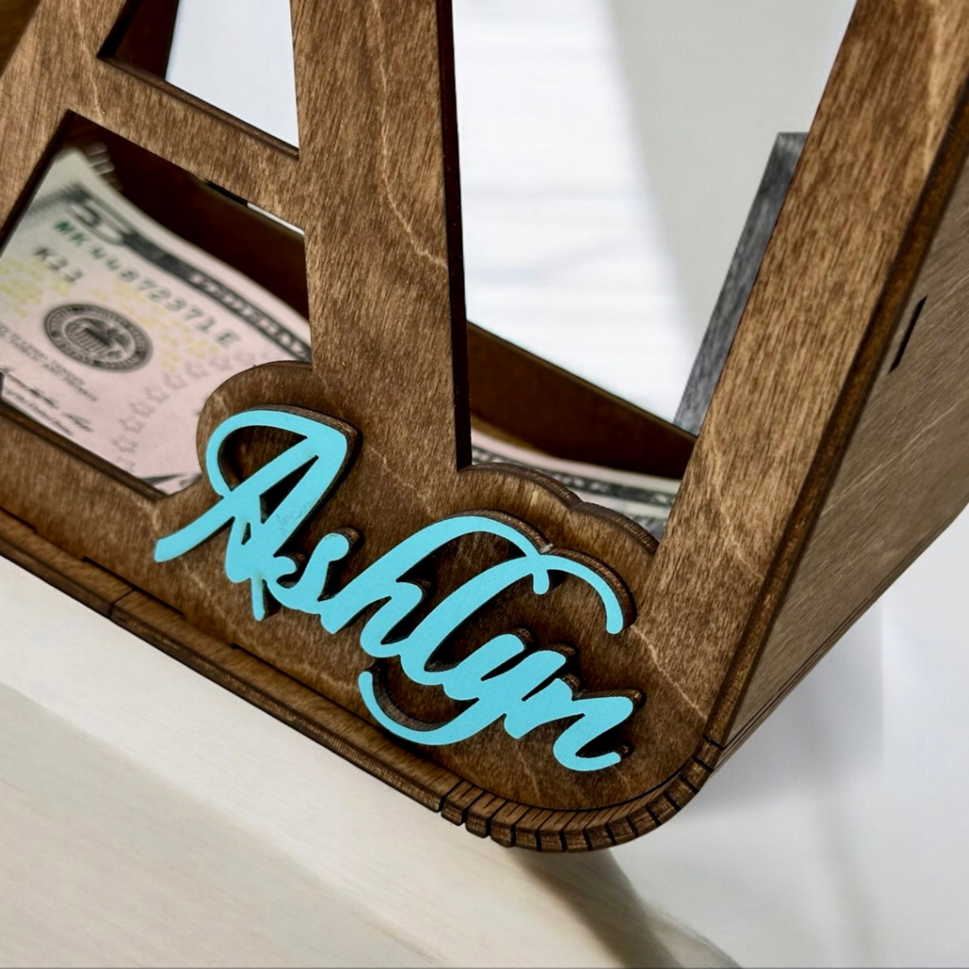 Wooden money box with 'Ashlyn' engraving and dollar bills inside