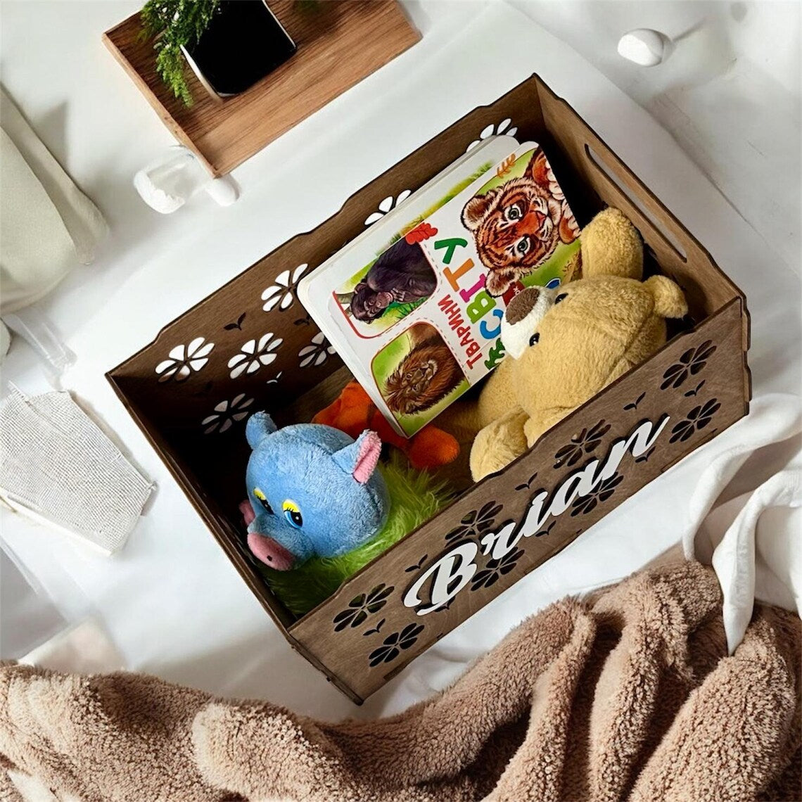 Wooden gift box with toys and a book inside, on a white surface.