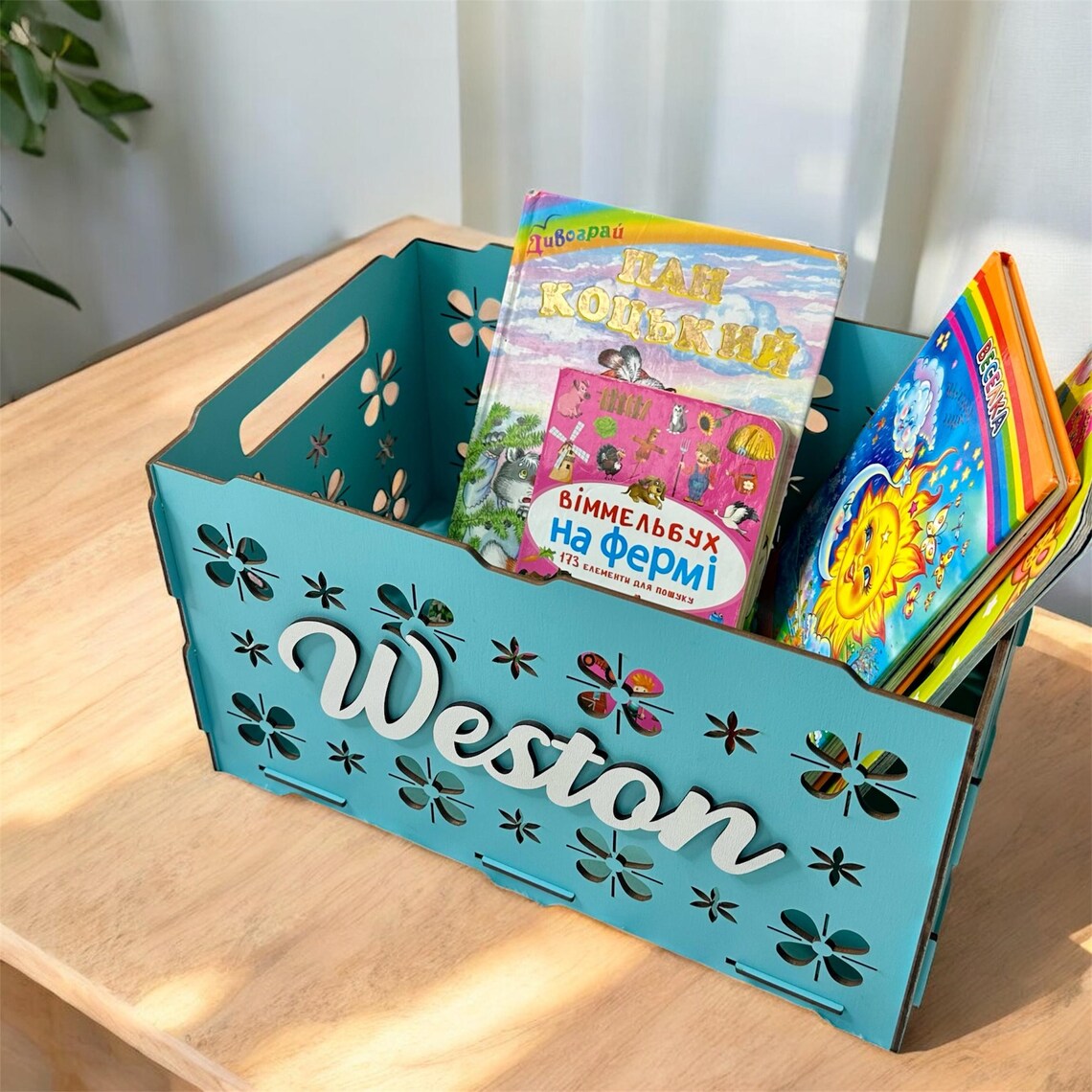 Teal storage caddy holding children's books on a wooden surface.