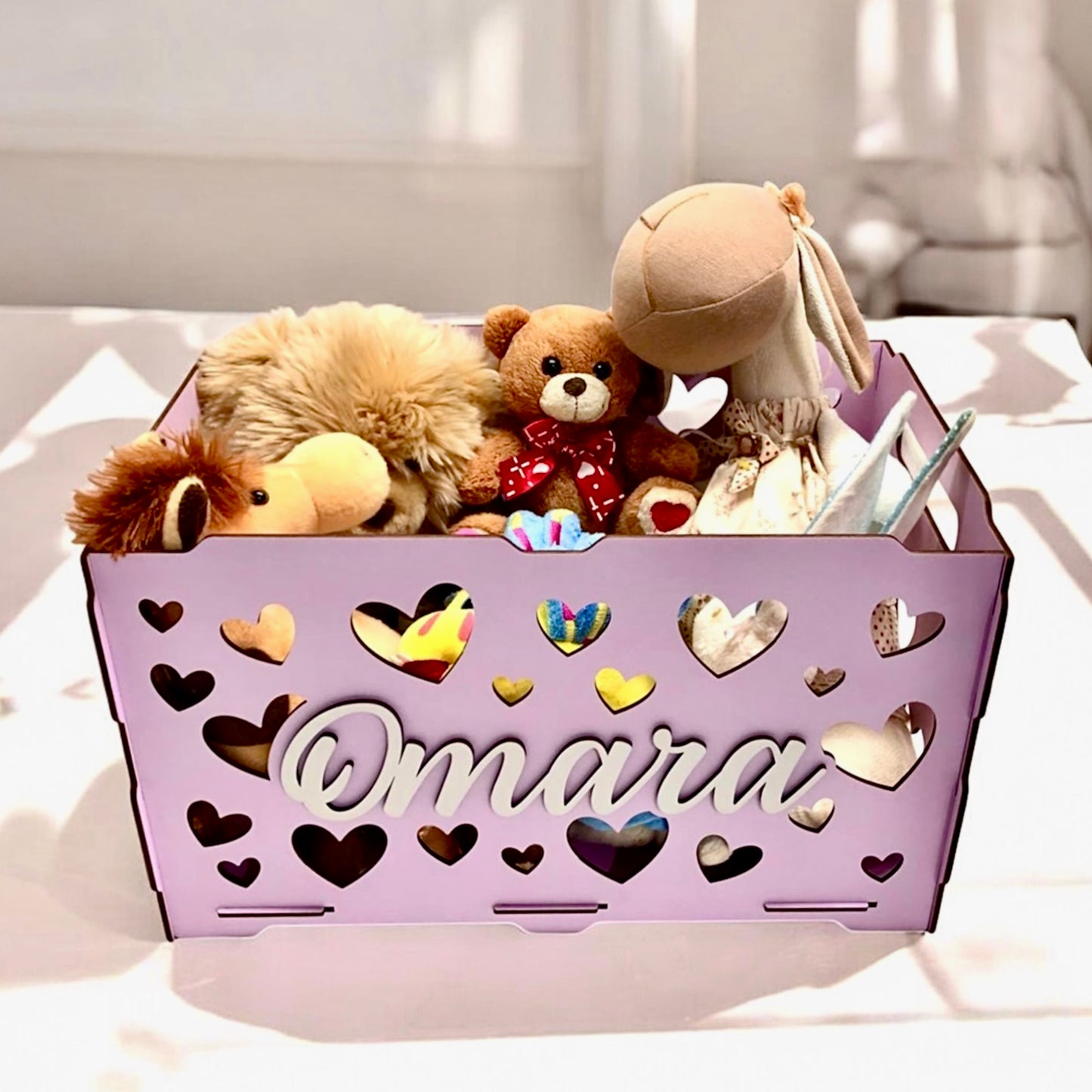Purple storage basket with heart designs and stuffed toys on a white surface