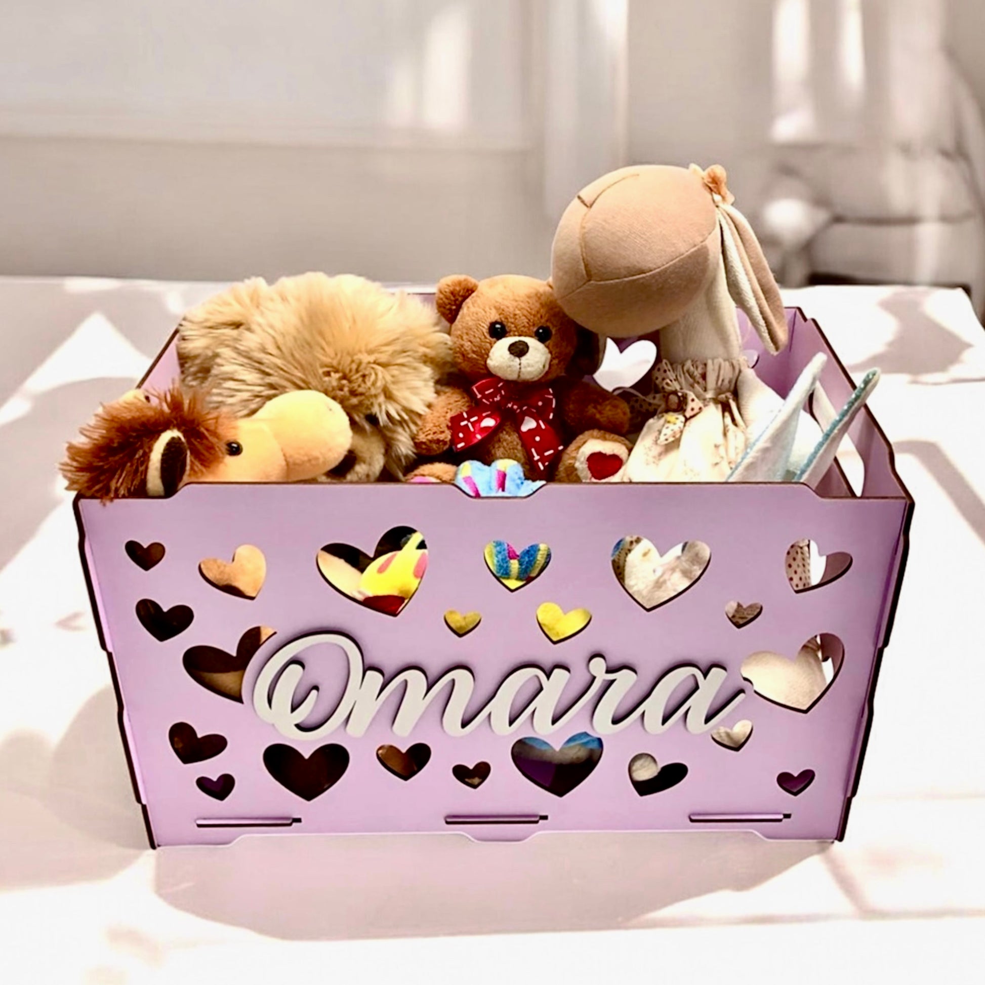 Purple storage basket with heart designs and stuffed toys on a white surface
